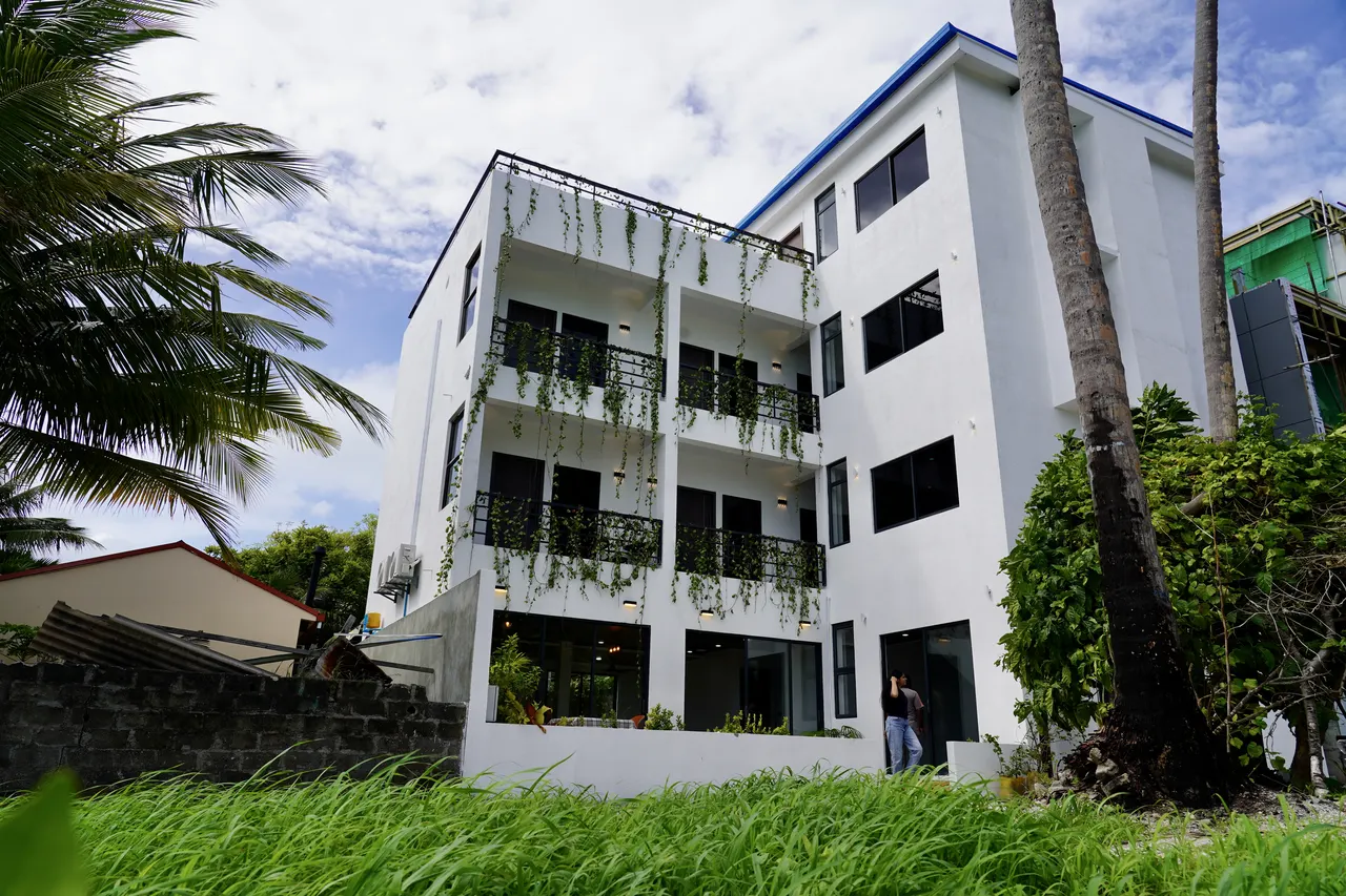 Cozy Art Dhangethi, a white four-storey boutique hotel with balconies and palm trees on Dhangethi island, South Ari Atoll
